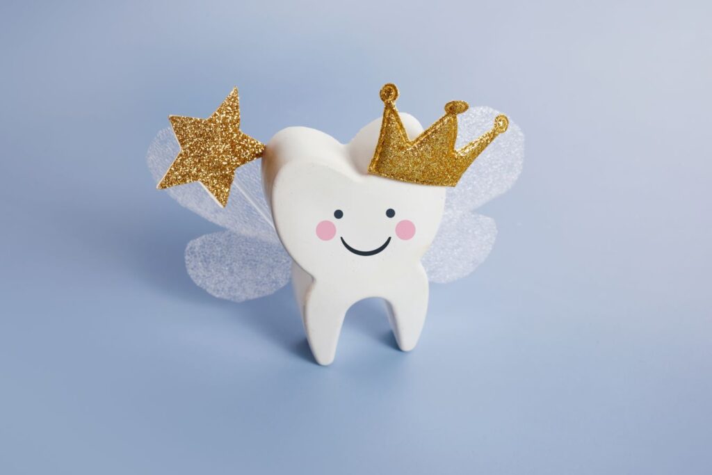 A smiling tooth figurine with a crown, wings, and a wand.