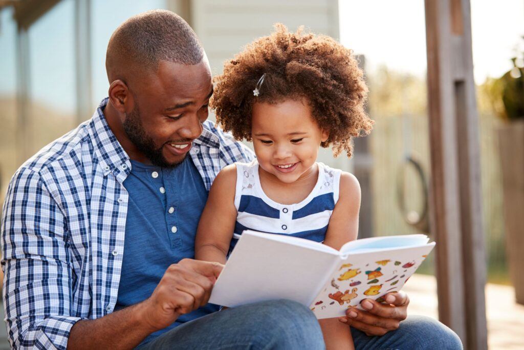 Man in blue shirt reading to little girl outside